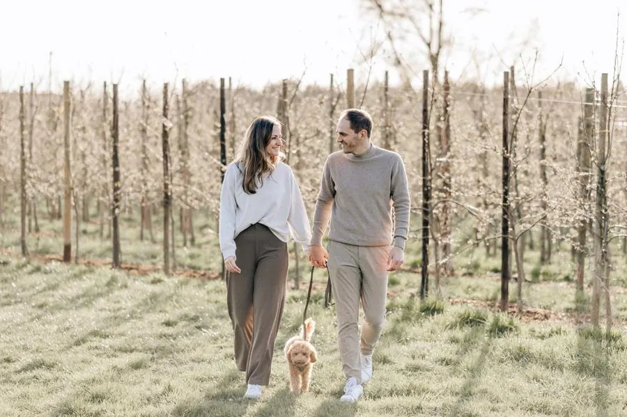 Paar in Creme und Beige spaziert mit Hund durch eine Obstplantage im Alten Land