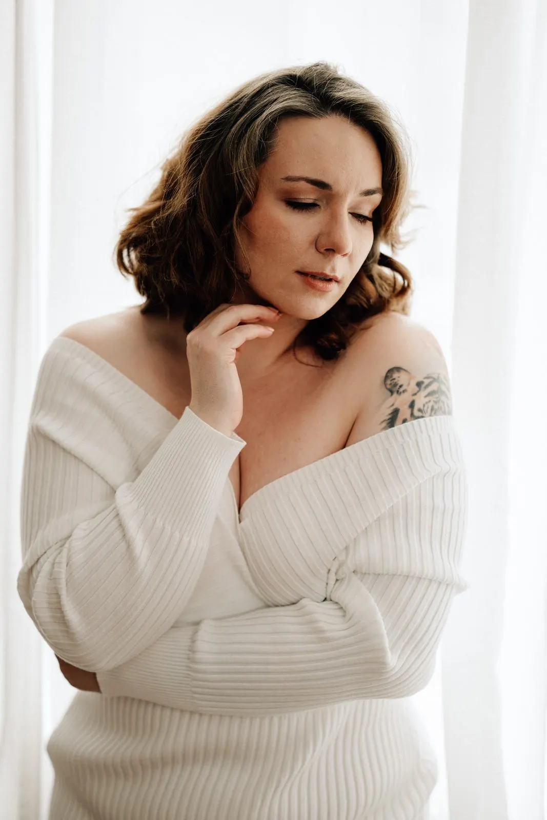 Frau im schulterfreien Rippstrickpullover mit gesenktem Blick