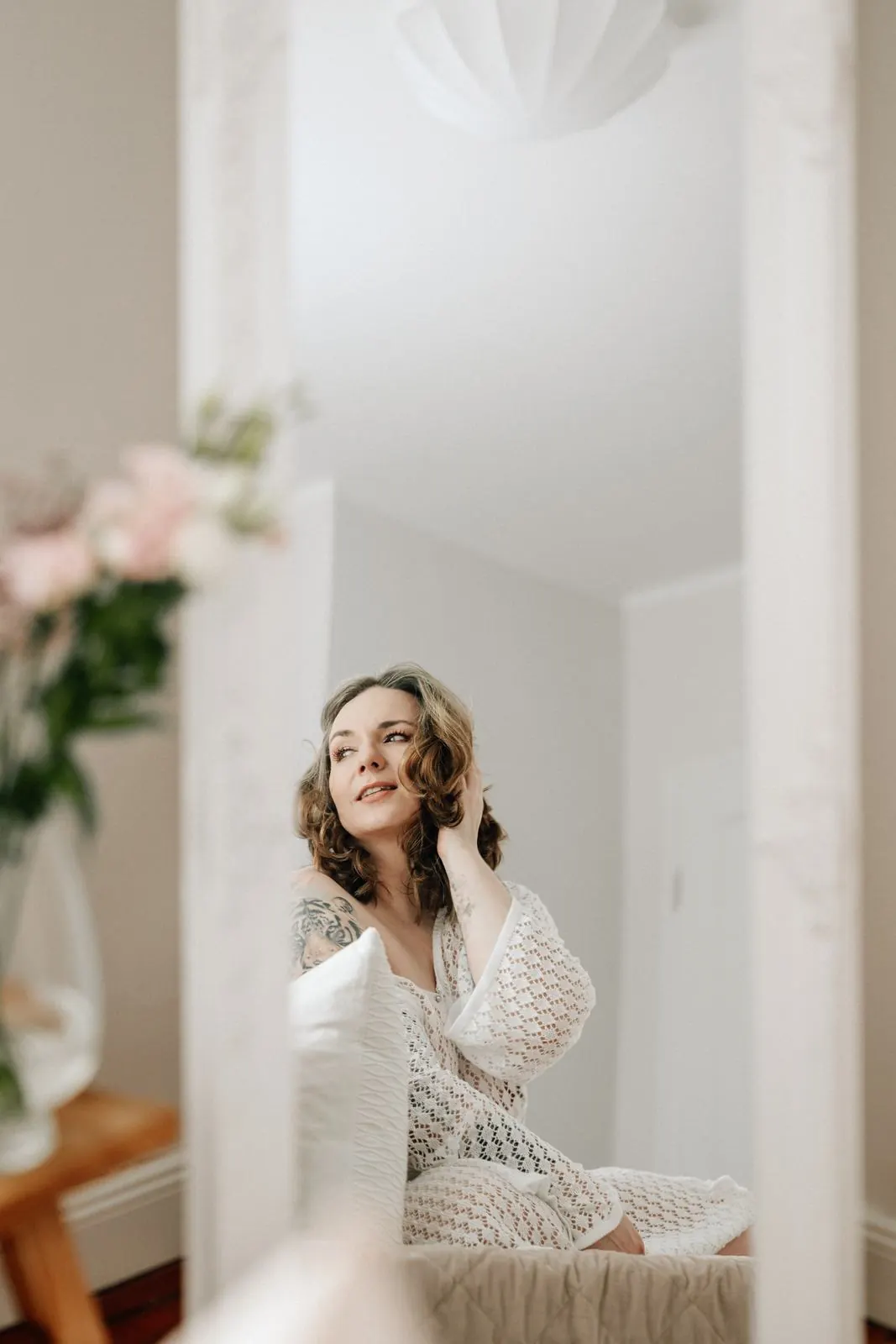 Spiegelbild einer lächelnden Frau im Häkelkleid, Blumen im Vordergrund