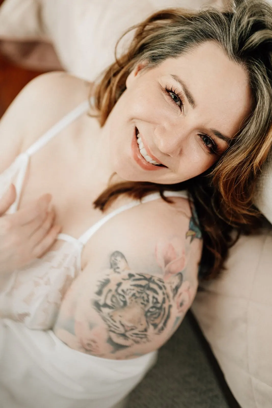 Frau liegt lachend auf dem Bett, Tiger-Tattoo auf der Schulter
