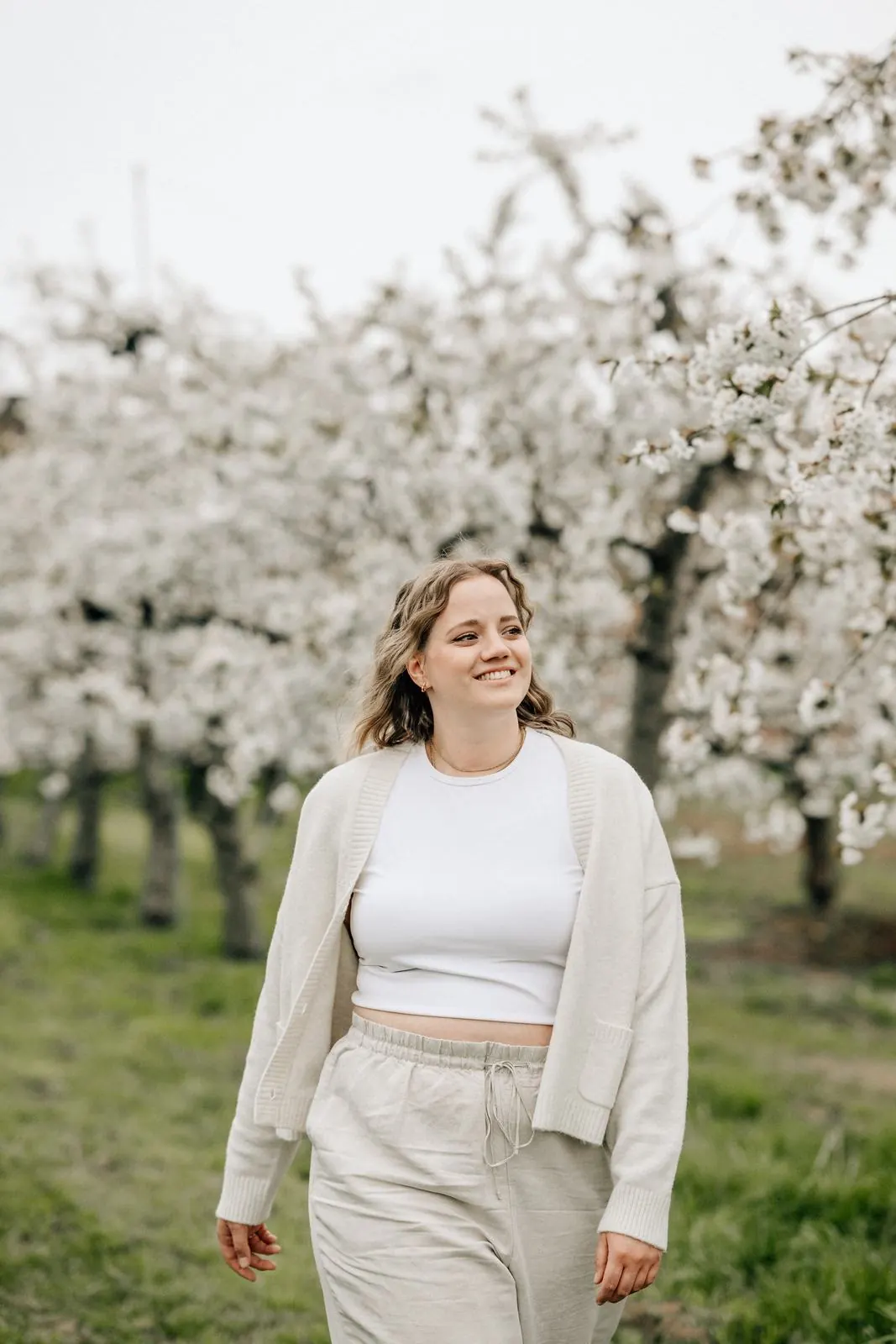 Frau in Creme lächelt beim Spaziergang durch die Kirschblüte
