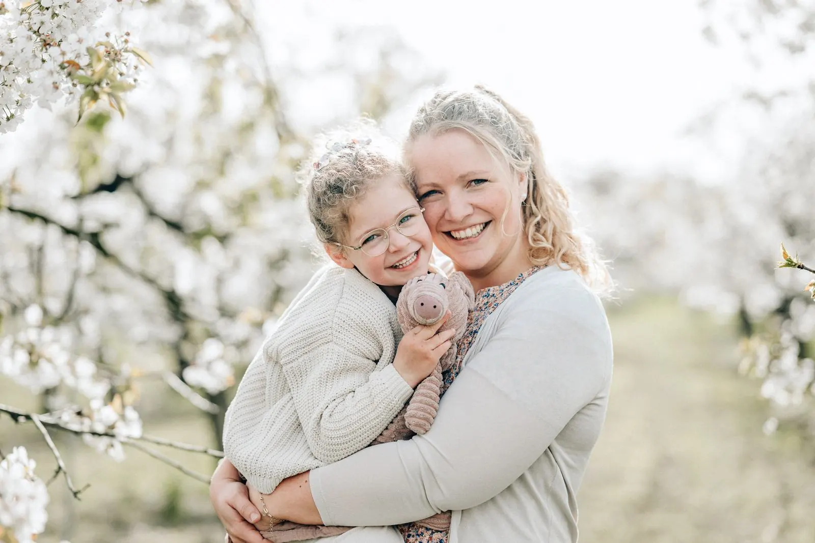 Mutter und Tochter mit Kuscheltier lachen in die Kamera, Obstblüte Jork