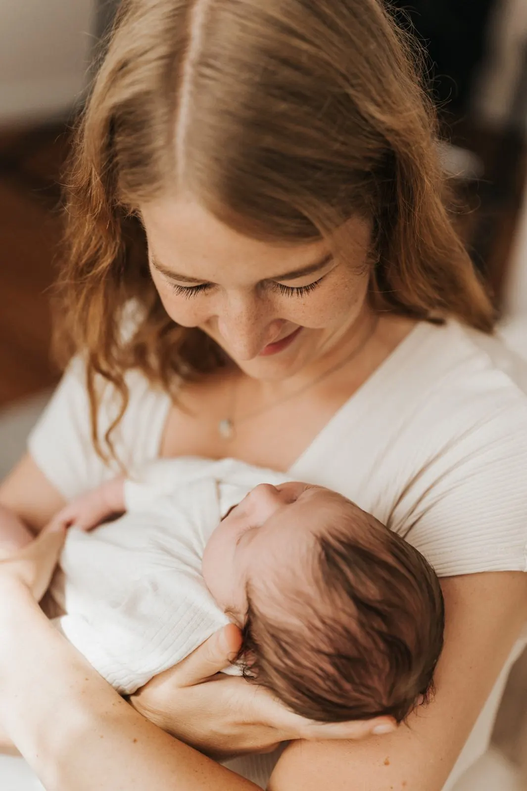 Mutter blickt lächelnd auf ihr schlafendes Neugeborenes im Arm