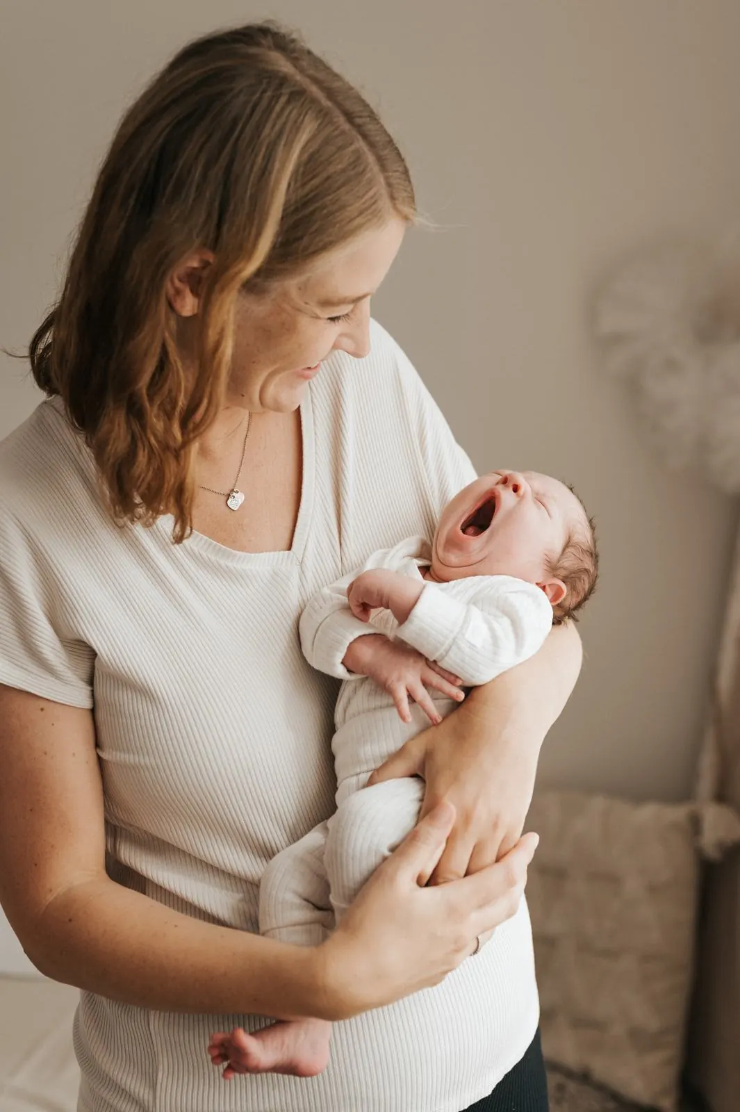 Neugeborenes gähnt im Arm seiner Mutter im hellen Studio