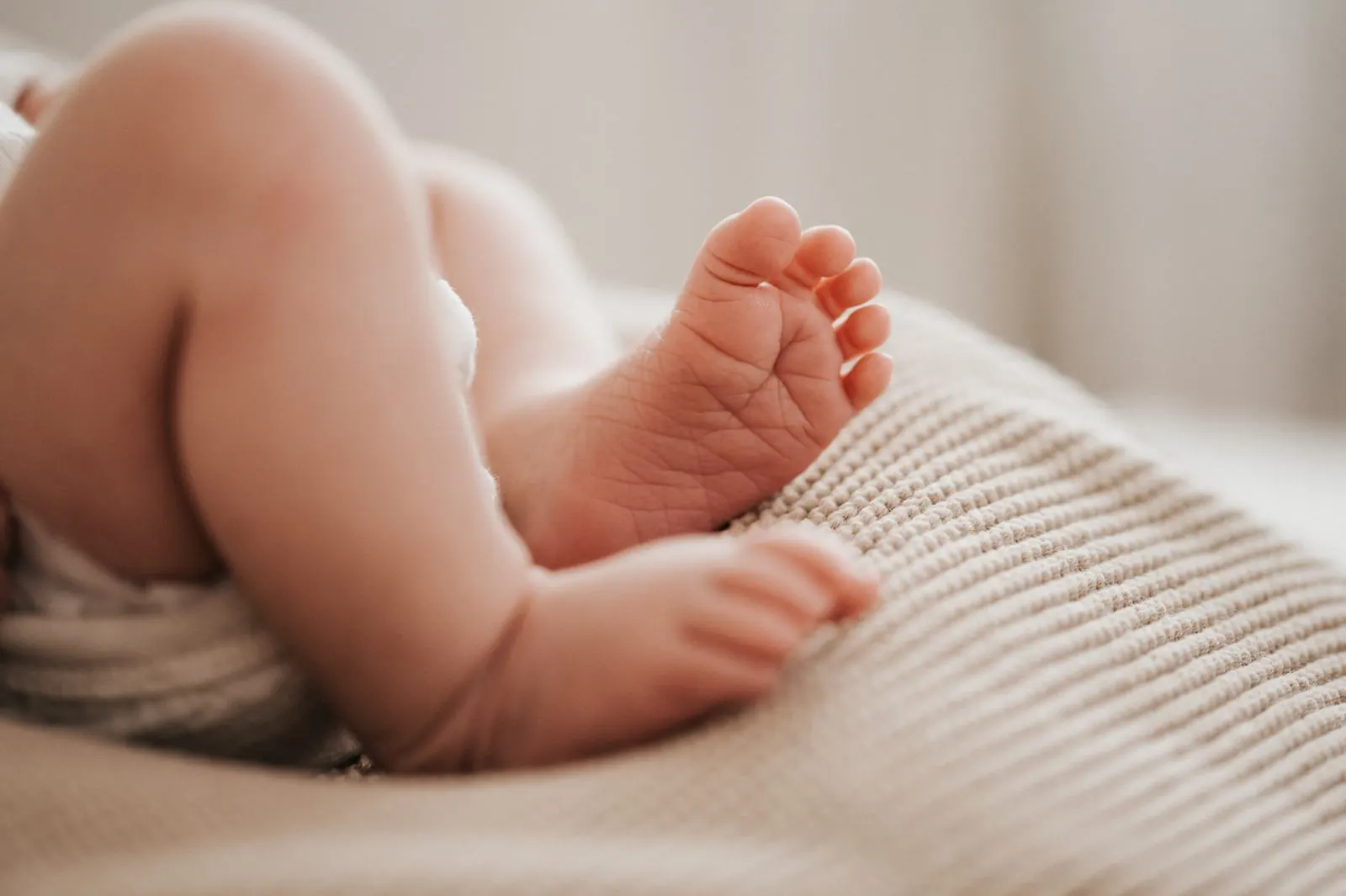 Winzige Füße eines Neugeborenen auf einer beigen Strickdecke