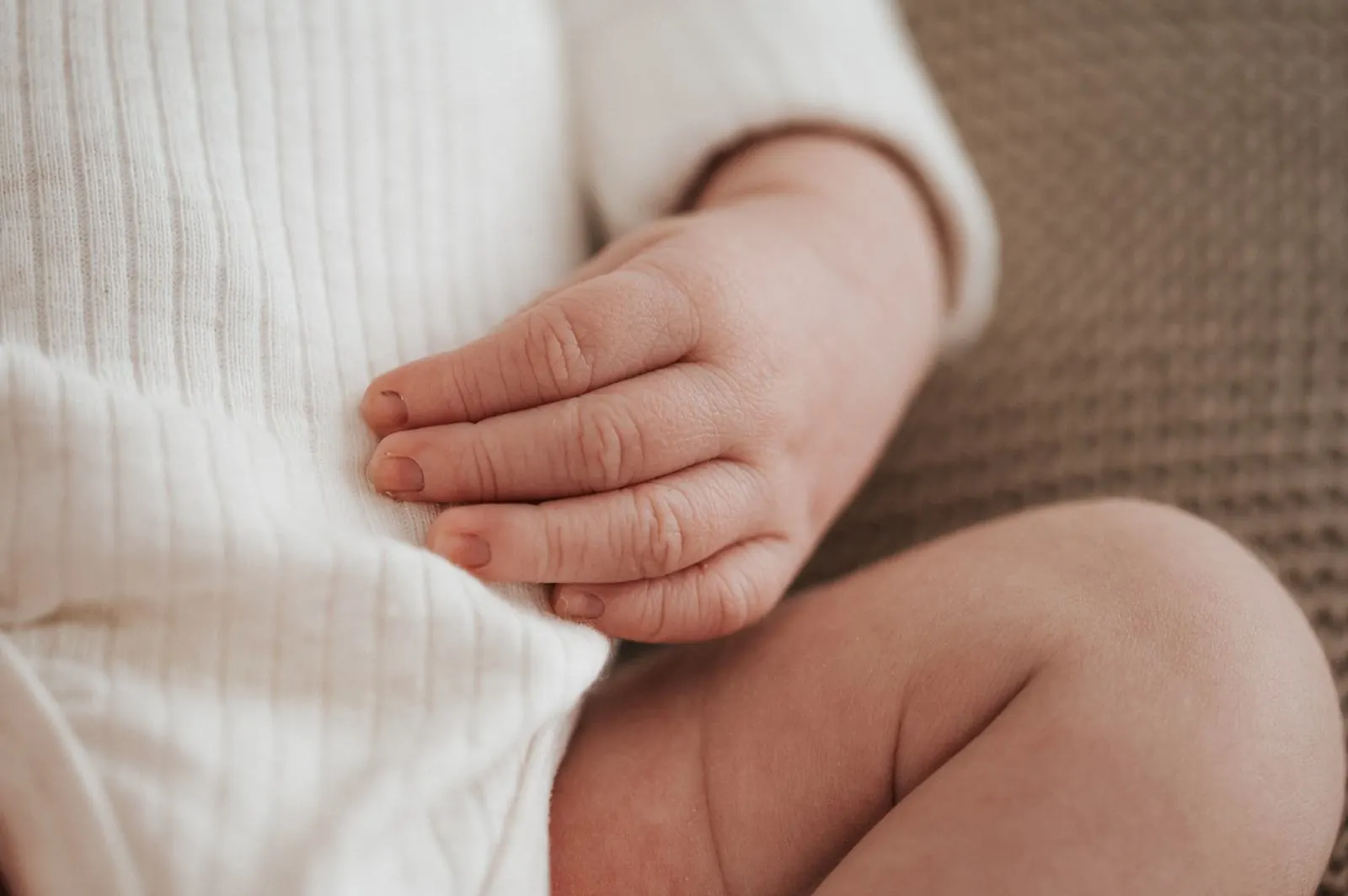 Kleine Hand eines Neugeborenen auf dem gerippten Body