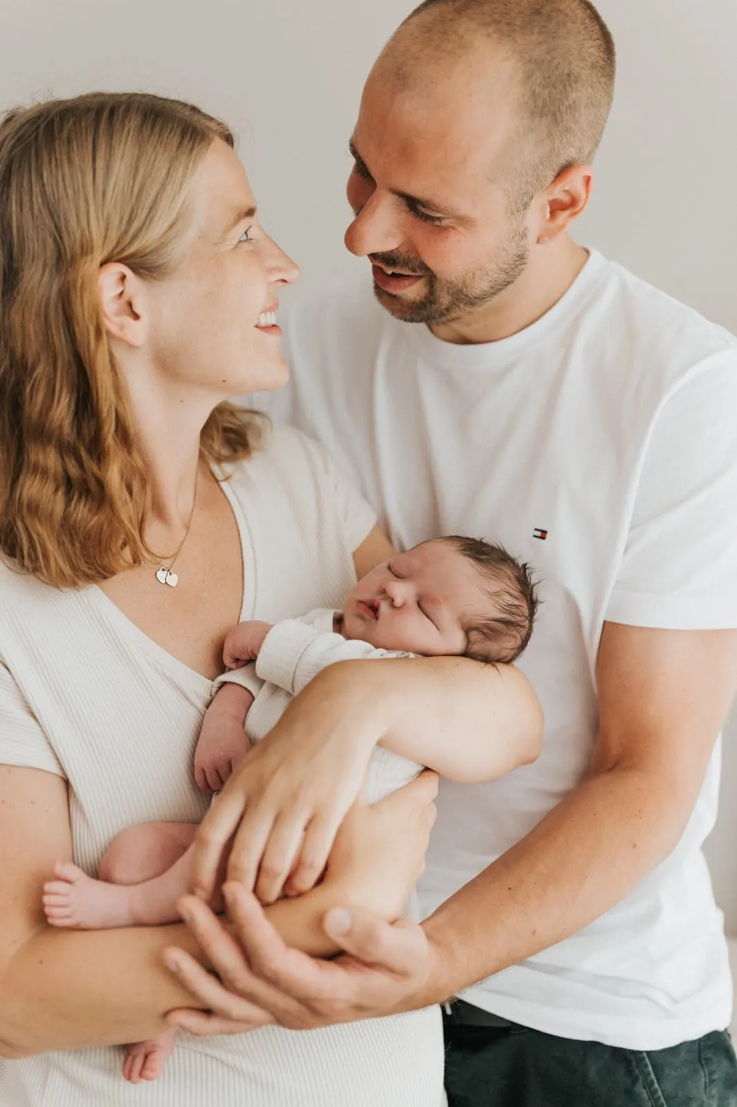 Eltern halten ihr Neugeborenes und lächeln sich an, Neugeborenenfotografie im Studio Jork