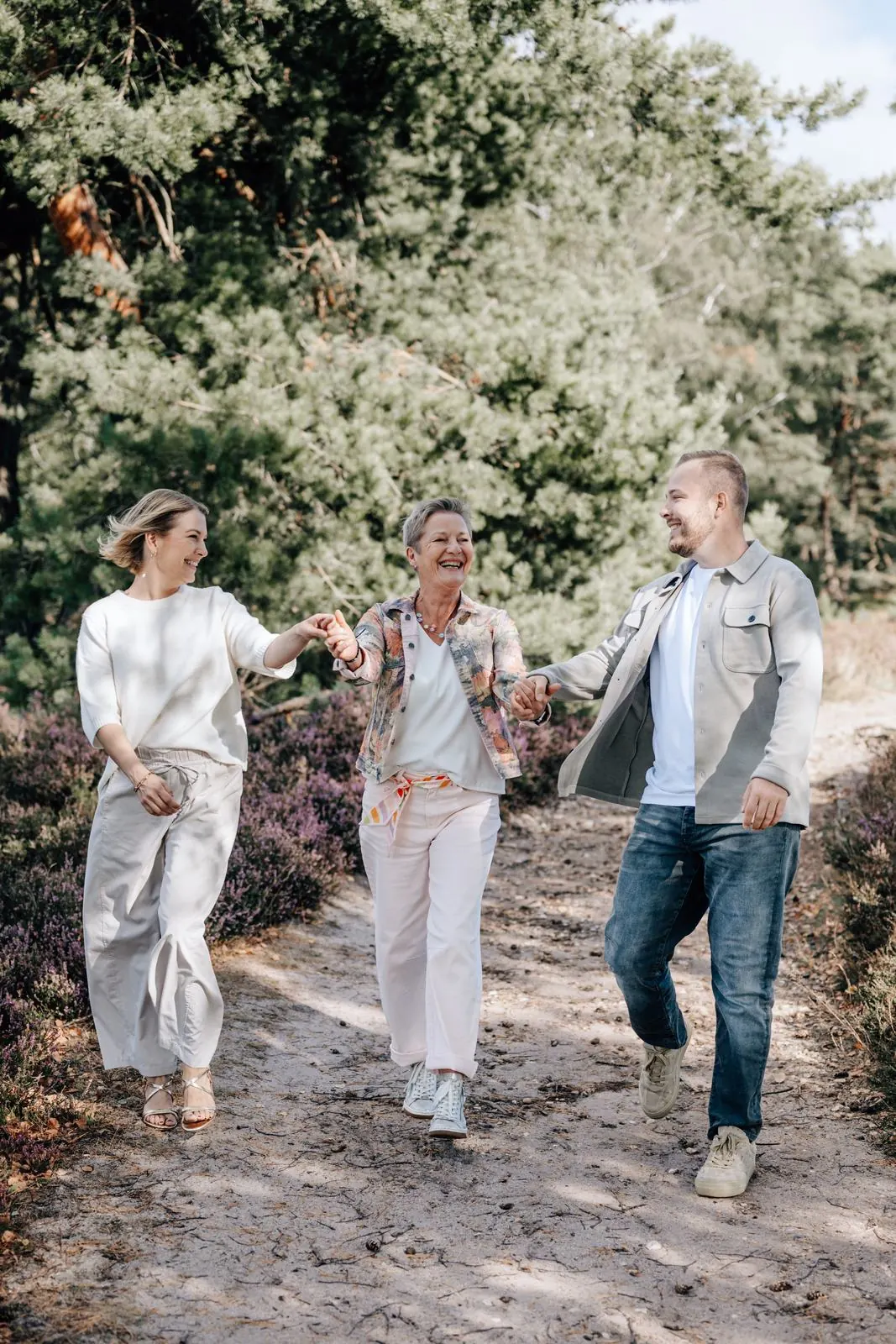 Drei Erwachsene laufen lachend Hand in Hand durch die Heide, Familienshooting Julia Aßmann