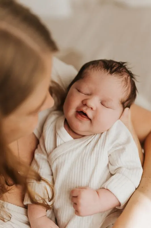 Baby lächelt schlafend in den Armen der Mutter, Neugeborenenfotografie im Studio Jork