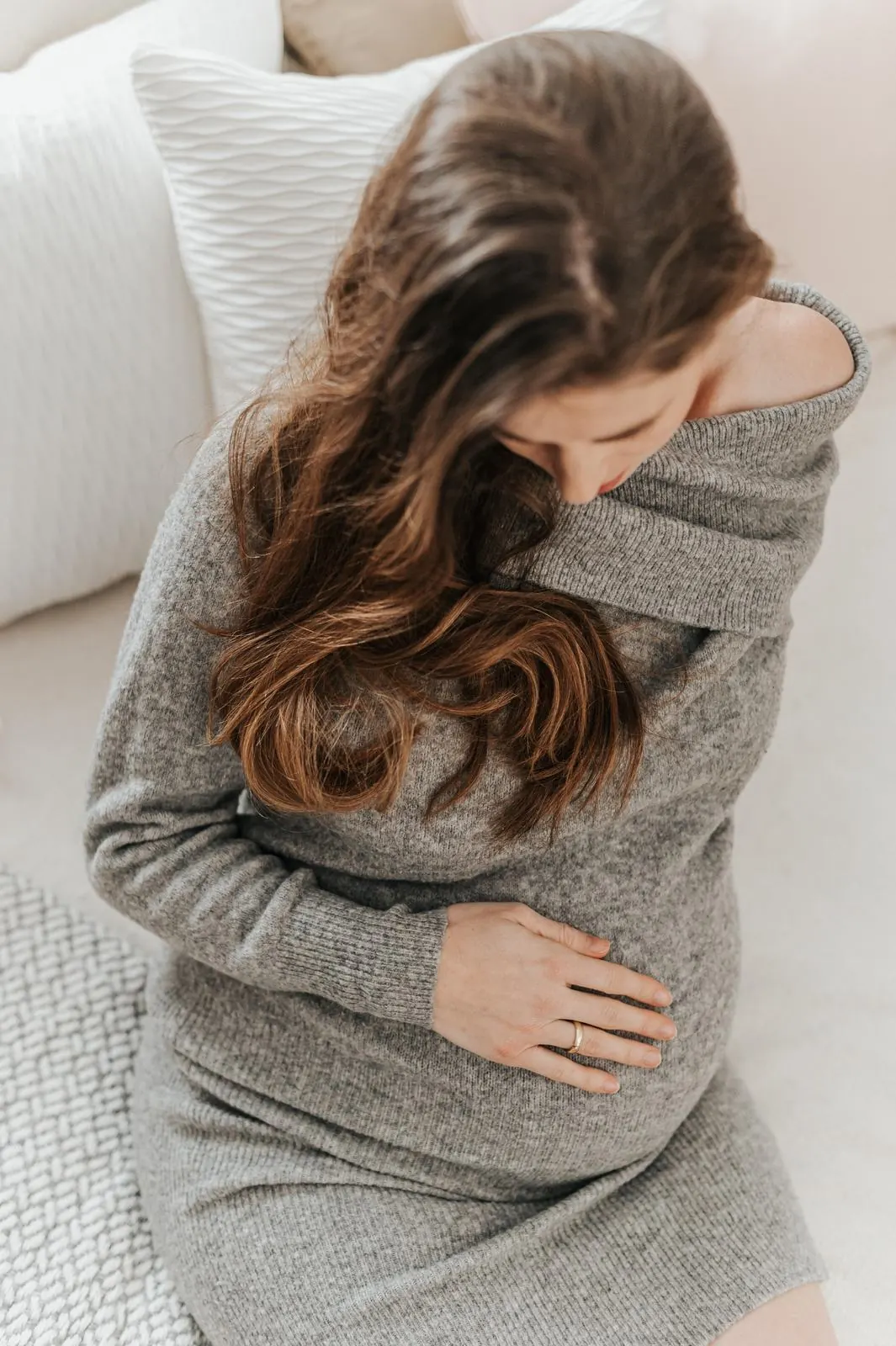 Schwangere im grauen Strickkleid hält ihren Babybauch, Schwangerschaftsfotografie im Studio Jork