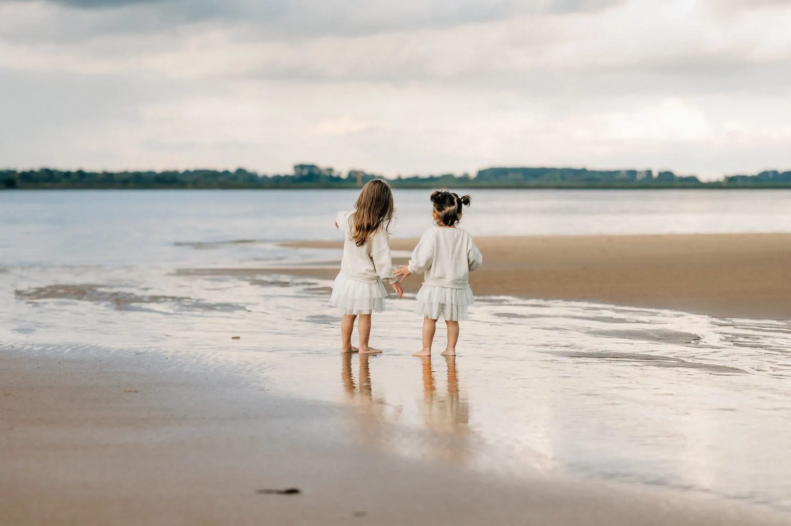Zwei kleine Schwestern stehen barfuß am Elbstrand und schauen aufs Wasser