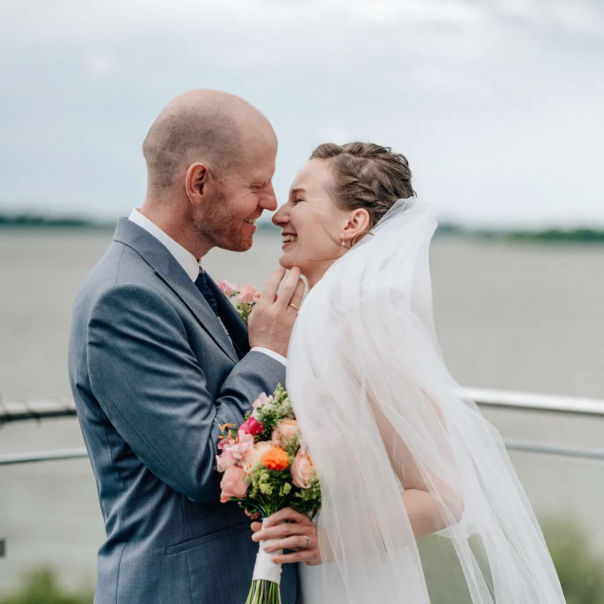 Brautpaar lacht sich an der Elbe an, der Schleier weht im Wind, Hochzeitsfotografie Julia Aßmann
