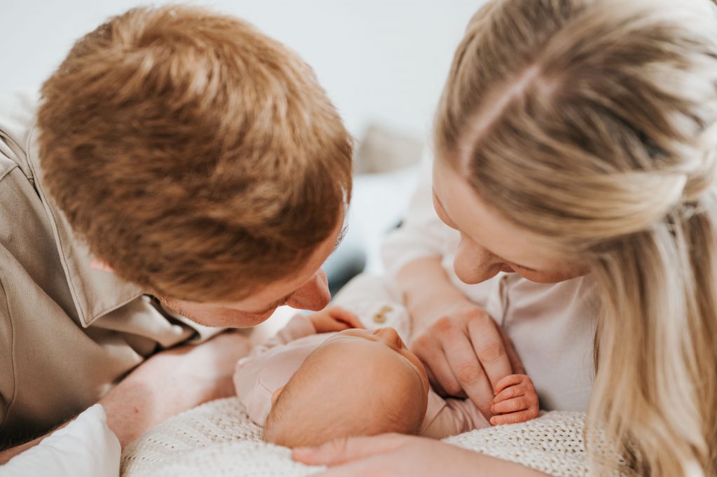 Eltern liegen mit ihrem Baby auf dem Bett im Fotostudio beim Neugeborenenshooting mit Julia Aßmann Fotografie in Jork für Stade und Umgebung.