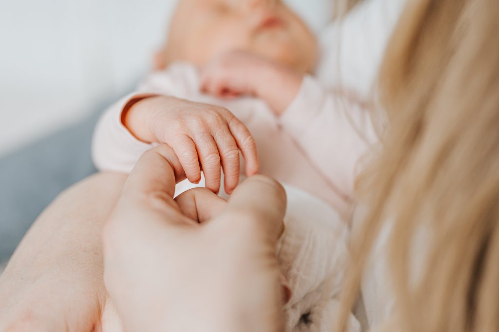 Nahaufnahme von der Hand eines Neugeborenen liegt auf dem Zeigefinger der Mutter im Fotostudio beim Neugeborenenshooting in Jork